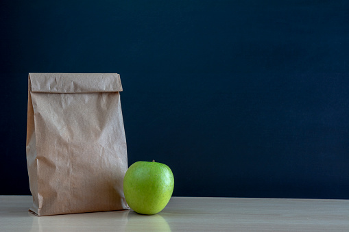 School lunch. Brown paper bag and  a green apple on blackboard background.