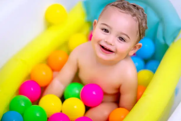 Portrait of a cute baby boy taking bath with many colorful balls, enjoying bathing process, happy healthy childhood, baby hygiene concept