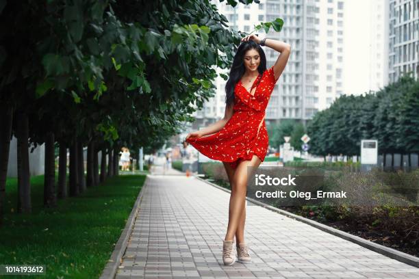 Nice Tanned Stylish Brunette Girl In Red Short Dress With Flowers Is Standing Poses And Flirting Walking On The Street City Stock Photo - Download Image Now