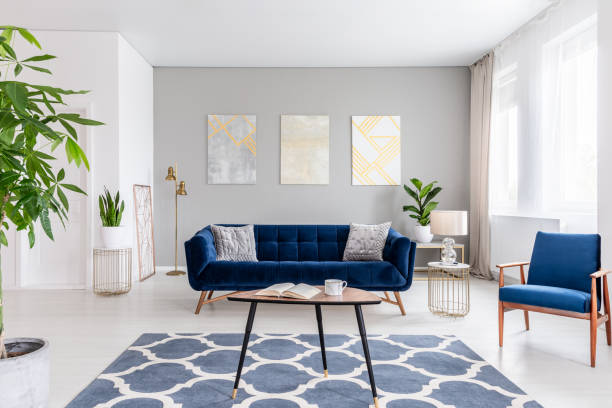 echtes foto von einem eleganten wohnzimmer interieur mit blauem sofa, sessel, couchtisch, gemusterten teppich und gemälde an der grauen wand - living room blue sofa carpet stock-fotos und bilder