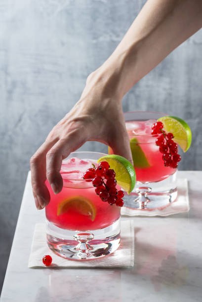 istock Woman's Hand Reaching for Cold Red Currant Caipirinha Cocktail on Marble Bar Counter 1014198742