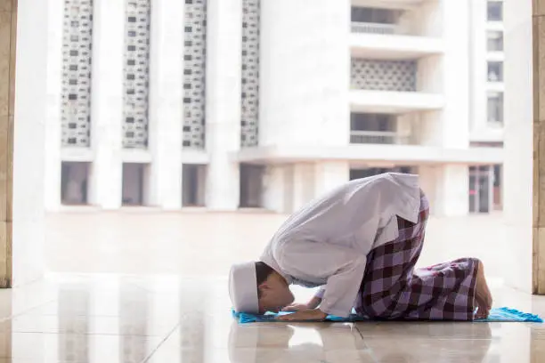Side view of young Muslim man posing prostration while doing Salat in the mosque