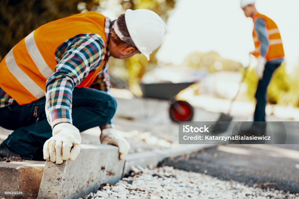 Worker with gloves and in helmet arranging curbs on the street Construction Industry Stock Photo