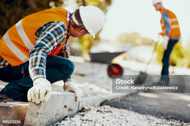 Worker With Gloves And In Helmet Arranging Curbs On The Street Stock Photo - Download Image Now