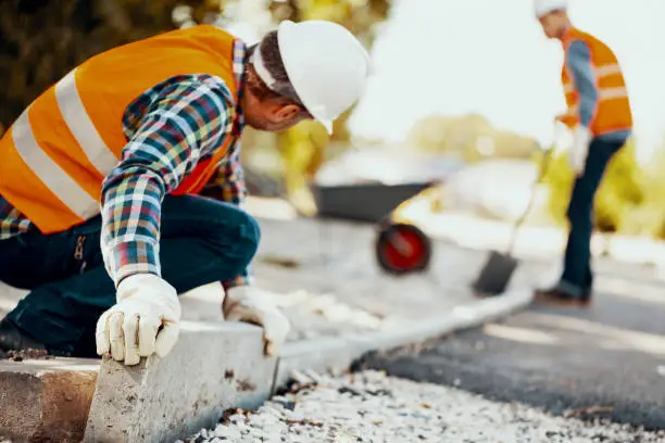 Photo of Worker with gloves and in helmet arranging curbs on the street