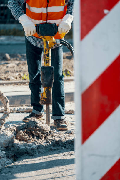istock Worker in reflective vest and with drill repairing asphalt during roadworks 1014212250