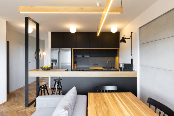istock Lights above countertop of black kitchen in open space interior with sofa and table. Real photo 1014216362