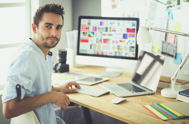 istock Portrait of young designer sitting at graphic studio in front of laptop and computer while working online 1014237698
