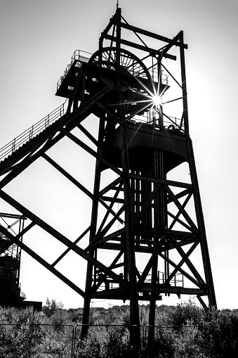 Silhouette of an Decaying, old, pit-head in South Wales. Black and white image with a specular starburst showing the stark death of a once vibrant industry and community.