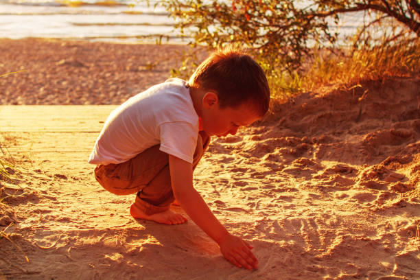 istock boy playing with sand on the beach. sunset 1014252158