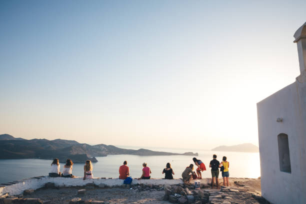 People On Top Of Plaka Village Watching The Sunset Milos island, Greece - June 12, 2018: Group of tourist sitting on top of the hill in Kastro to watch an amazing sunset. Kastro is the highest spot of Plaka, the capital of Milos. plaka athens stock pictures, royalty-free photos & images