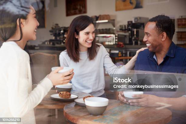 Three Friends Having Coffee And Laughing At A Coffee Shop Stock Photo - Download Image Now