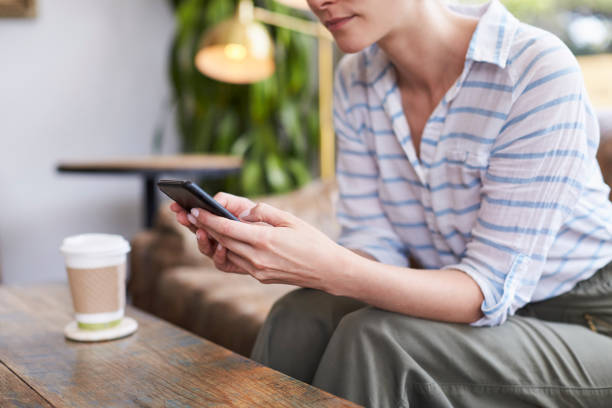 istock Young woman using smartphone in a coffee shop, mid section 1014261366