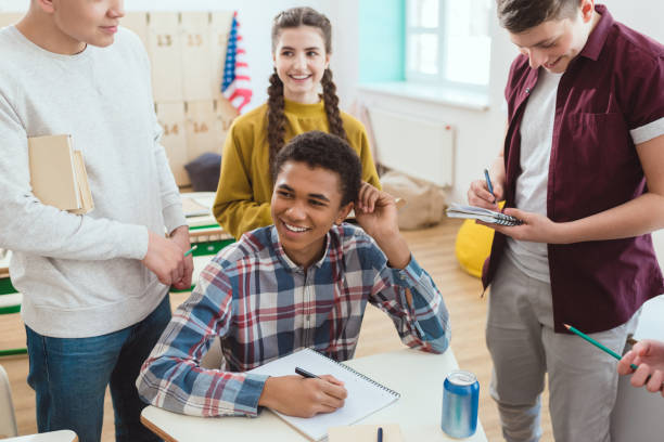 istock happy african american schoolboy writing in notebook while his classmates standing around 1014263826
