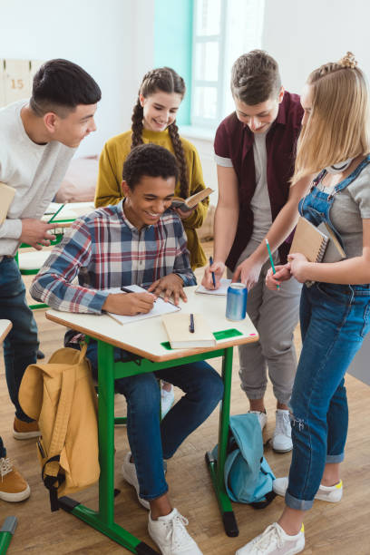 istock african american schoolboy writing in notebook while his classmates standing around 1014266164