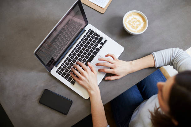 istock Young white woman using laptop at coffee shop, overhead view 1014266946