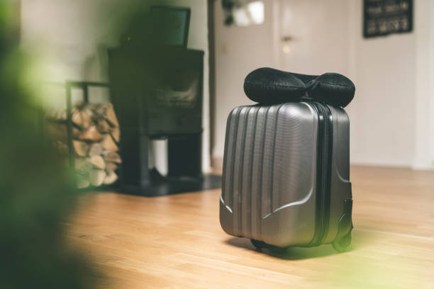 A packed suitcase and a black travel neck pillow are resting on the floor in someones home.