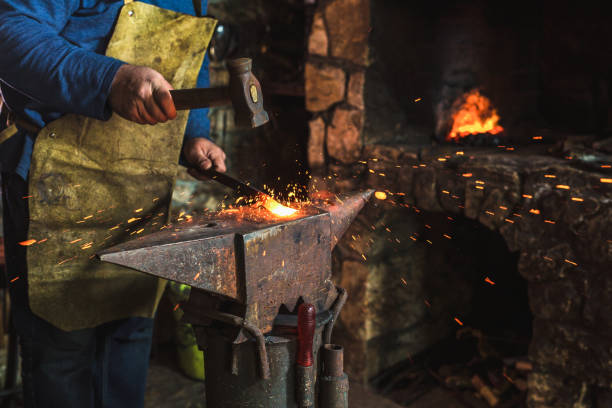 istock Blacksmith manually forging the molten metal on the anvil in smithy with spark fireworks, close up 1014297572