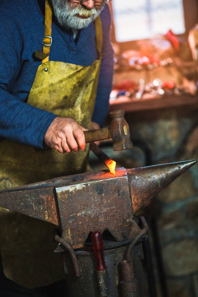 istock Blacksmith manually forging the molten metal on the anvil in smithy with spark fireworks, close up 1014297676