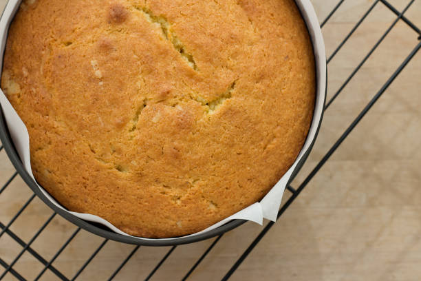 Madeira cake on a Cooling Rack A round shaped Madeira cake in a baking tin, parchment paper on a wire cooling rack. cooling rack photos stock pictures, royalty-free photos & images