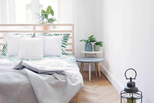 istock Modern scandinavian sunny bedroom with plants , floral pattern bedding and pilows. Space with white walls and brown wooden parquet. 1014312912