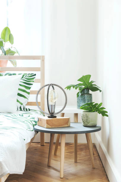 istock Modern and stylish bedroom with plants, design lamp and floral pattern bedding. Bright and sunny space with wooden parquet and white walls. 1014312982