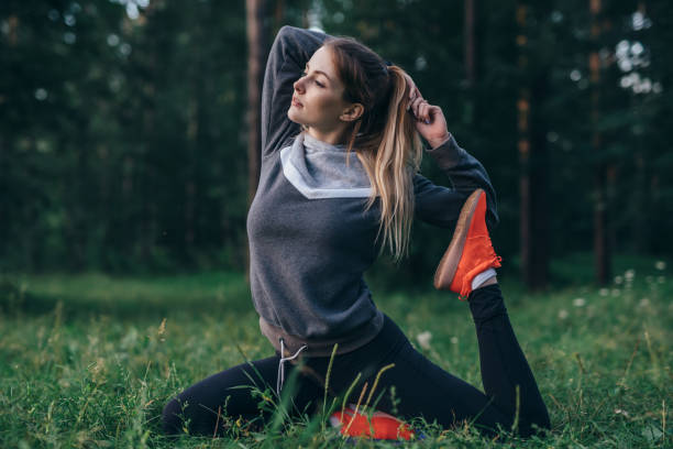 istock Young woman practicing yoga doing one-legged pigeon pose sitting on grass in park 1014322672