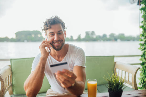 istock Happy young man talking on mobile phone and looking at credit card 1014328022