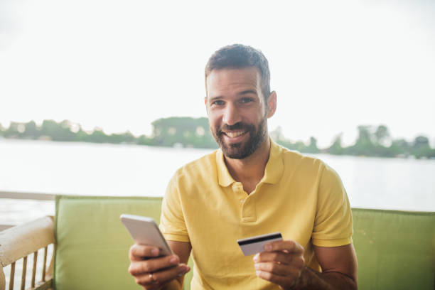 istock Young man with mobile phone and credit card in his hands smiling 1014332230