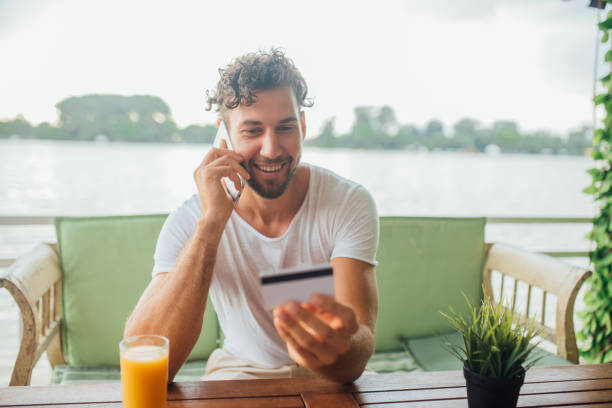 istock Smiling man looking at credit card while talking on mobile phone 1014332910