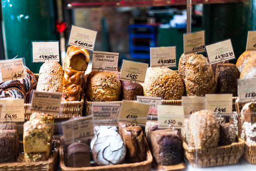 Close up color image depicting a large selection of artisan gourmet breads and pastries displayed on a bakery stall at a popular food market in London, UK, one of the most popular and oldest food markets in the world in fact. Each item is labelled and priced. Room for copy space.