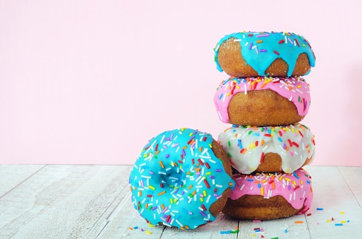 Stack of donuts with pastel colored icing on a soft pink background