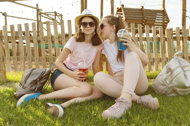 adolescentes meninas 14,15 anos se divertir em uma zona de lazer e entretenimento. eles se sentam no gramado, bebidas, conversa e segredo. - 16 17 years - fotografias e filmes do acervo