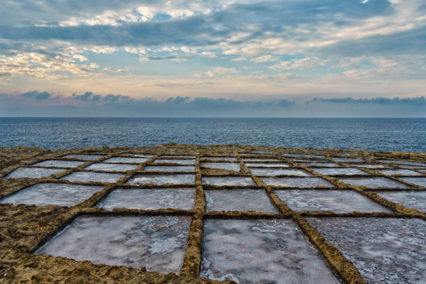 Mediterranean Salt pans at Qbajjar, Gozo at sunset. Reflection and salt crystals visible.