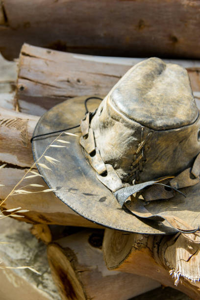 istock Handcrafted artisan old leather hat lying on wood logs in forest prepared for making fire. Warm earthy brown grey yellow tones. Hiking camping wanderlust unity with nature concept. Lifestyle image 1014399178