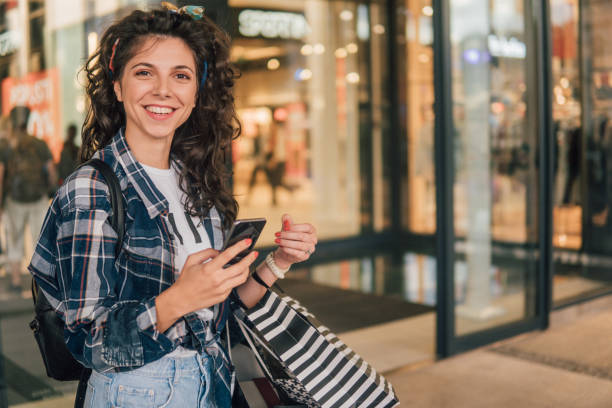 istock Smiling woman using mobile phone while carrying shopping bags 1014418284
