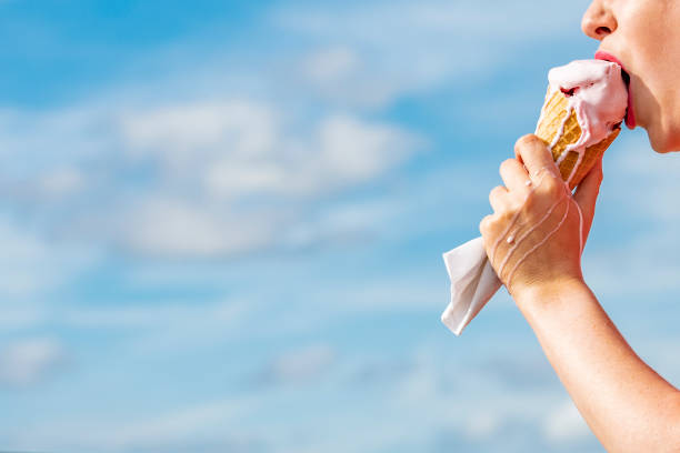 istock Mouth eating Ice-cream Cone against blue sky. 1014421830