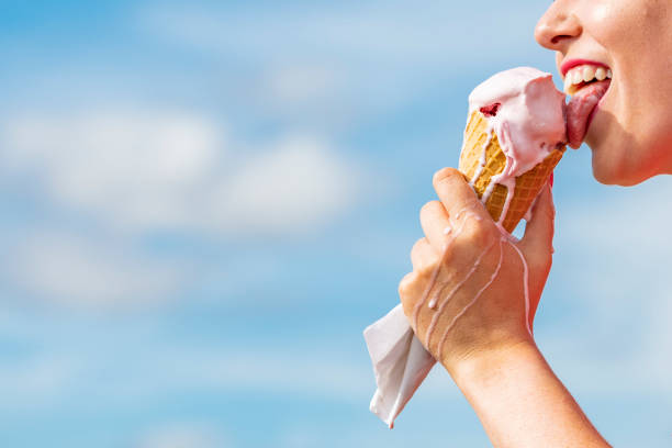Mouth eating Ice-cream Cone against blue sky.