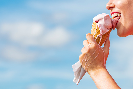 Mouth eating Ice-cream Cone against blue sky.