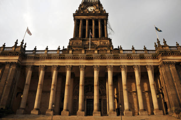 una visión gran angular de la parte delantera del pasillo de ciudad de leeds con altas columnas de piedra torre del reloj y banderas en la luz del sol - leeds england leeds town hall town uk fotografías e imágenes de stock