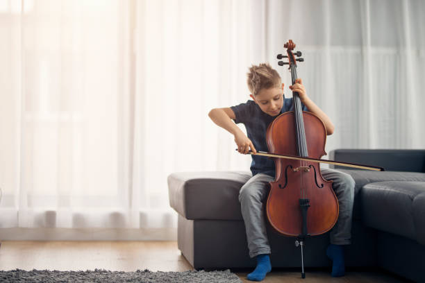 маленький мальчик, практикующий виолончель дома - cello стоковые фото и изображения