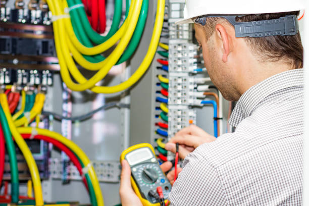 An electrical engineer measures the voltage in the electrical cabinet. A working electrician with a multimeter performs service work. stock photo