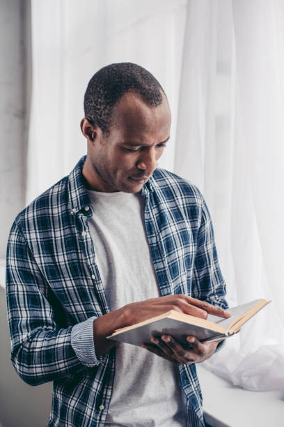 istock focused young african american man standing and reading book 1014429730