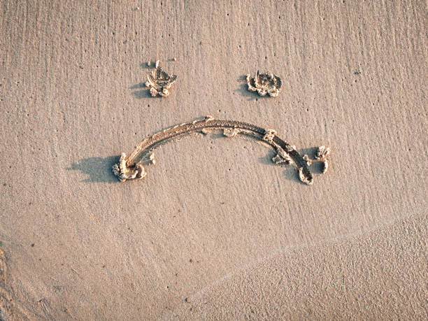 A sad smiley drawn on the sand. Depression concept. Anthropomorphic smiley face.