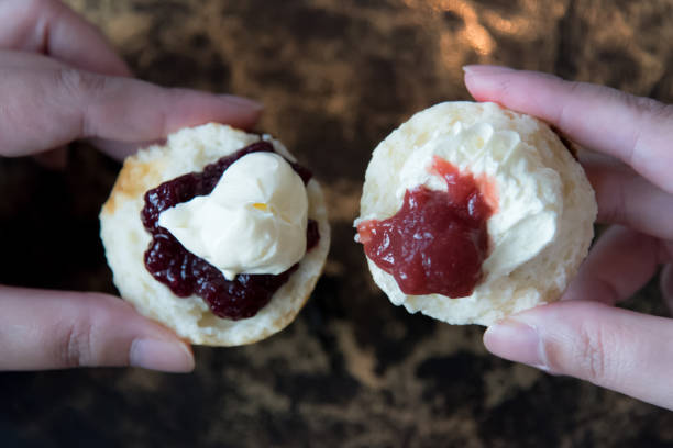 azjatka posiada pół split świeżo upieczony scone rozprzestrzeniania się z dżemem pierwszy, cornish sposób na lewej ręce i drugą połowę scone z kremem skrzepnięty pierwszy, devon sposób na prawej ręce. - cornish cream tea zdjęcia i obrazy z banku zdjęć