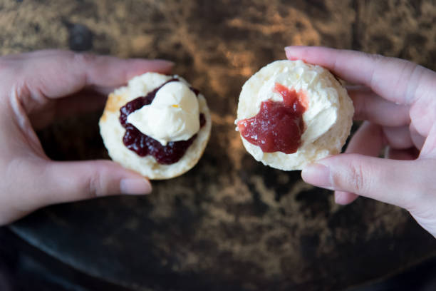 femme asiatique cale demi split scone fraîchement cuit parsemé de façon première, cornish de confiture sur sa main gauche et l’autre moitié de scone avec crème caillée tout d’abord, devon way sur sa main droite. - cornish cream tea photos et images de collection