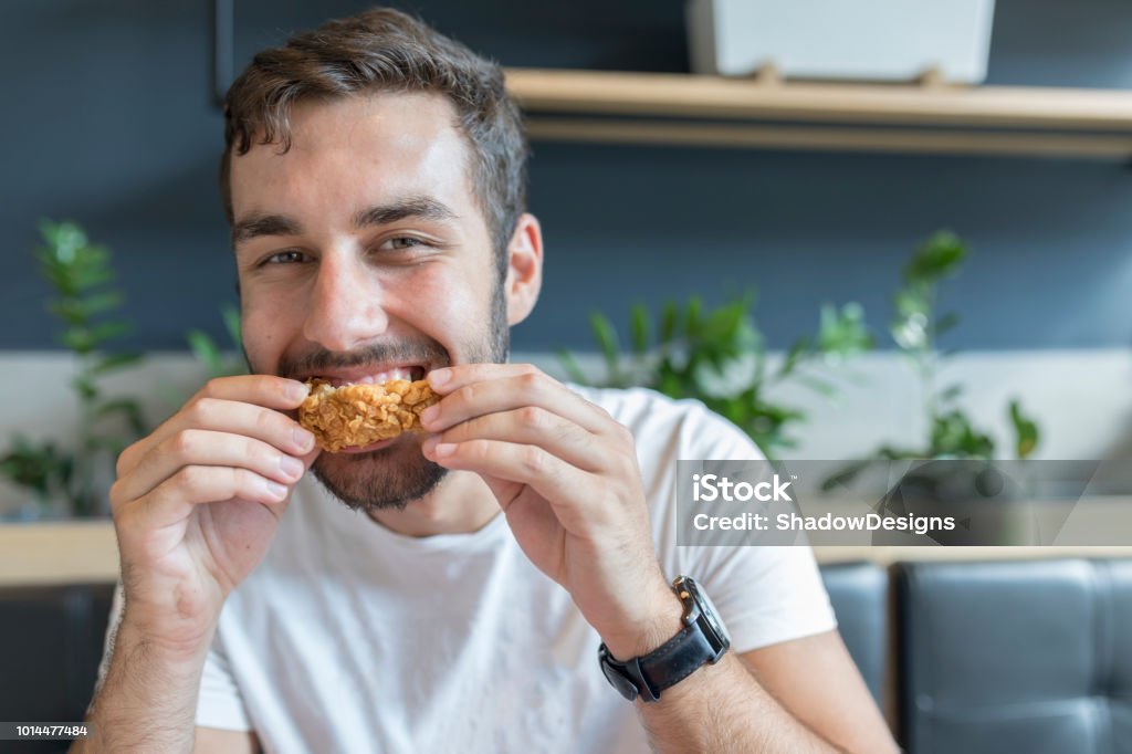 Giovane adulto che mangia ali di pollo durante la pausa pranzo - Foto stock royalty-free di Mangiare