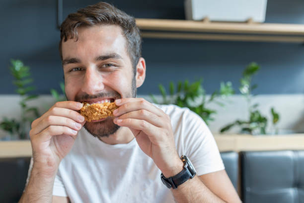 giovane adulto che mangia ali di pollo durante la pausa pranzo - man eating foto e immagini stock