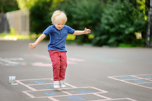 Child playing hopscotch on playground outdoors on a sunny day. Activities for preschooler kids.
