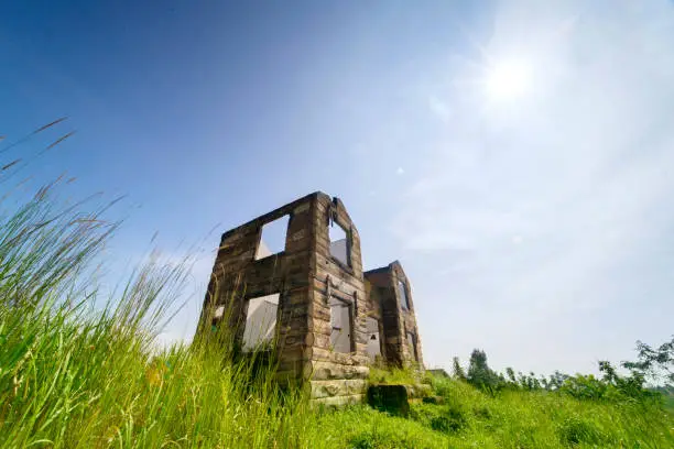 Low angle view of beautiful abandoned house overgrown with bushes under blue sky